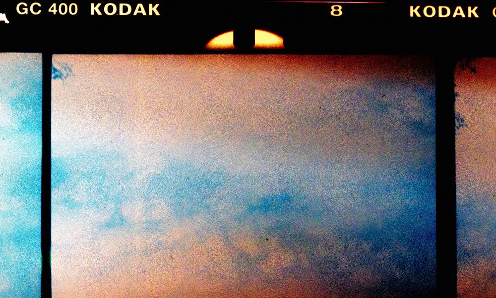 A close up of a 35mm film strip showing abstract cloud like image in pink and blue.