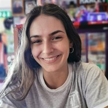 Head and shoulders photo of a smiling young woman with long brown hair and wearing a light grey t-shirt