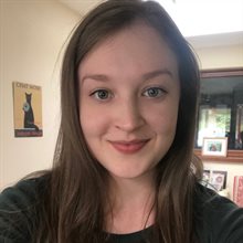 Smiling profile picture of a young white woman with long brown hair indoors