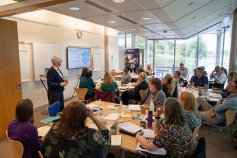 All participants from cohort 1 sitting around tables in a meeting room listening to a presentation during a residential