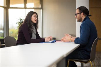 Man and woman sitting opposite each other at a table with notepads and folders on it having a discussion