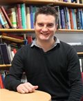Mark Bradley sits at a table in front of a packed bookshelf