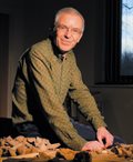 Will Bowden sits by a table, which is covered in fragments of objects
