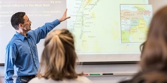 A man points at a PowerPoint slide in a classroom.
