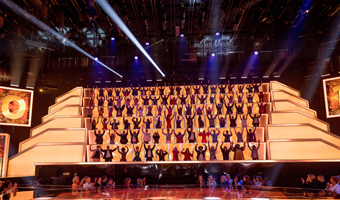 On the set of at All Together Now, with people in rows on a stage dancing with their arms in the air