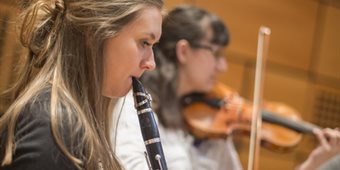 A student playing clarinet and another playing violin in the background