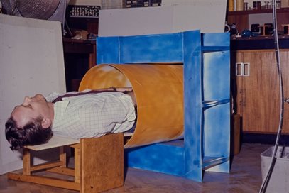 Colour photo of Peter Mansfield lying inside a mock-up of an MRI scanner. This image is from the papers of Peter Mansfield, held by Manuscripts and Special Collections. Document reference PPM/15/78/11.