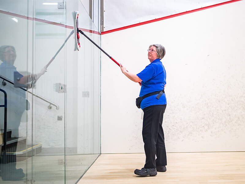 One of the cleaning team wiping the glass on a squash court at David Ross Sports Village