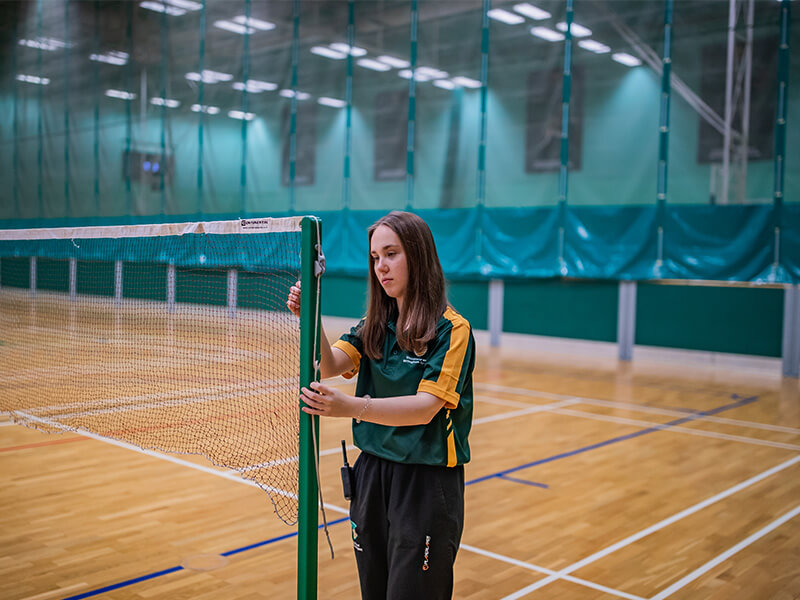 A sports assistant helping to set up a badminton net at David Ross Sports Village