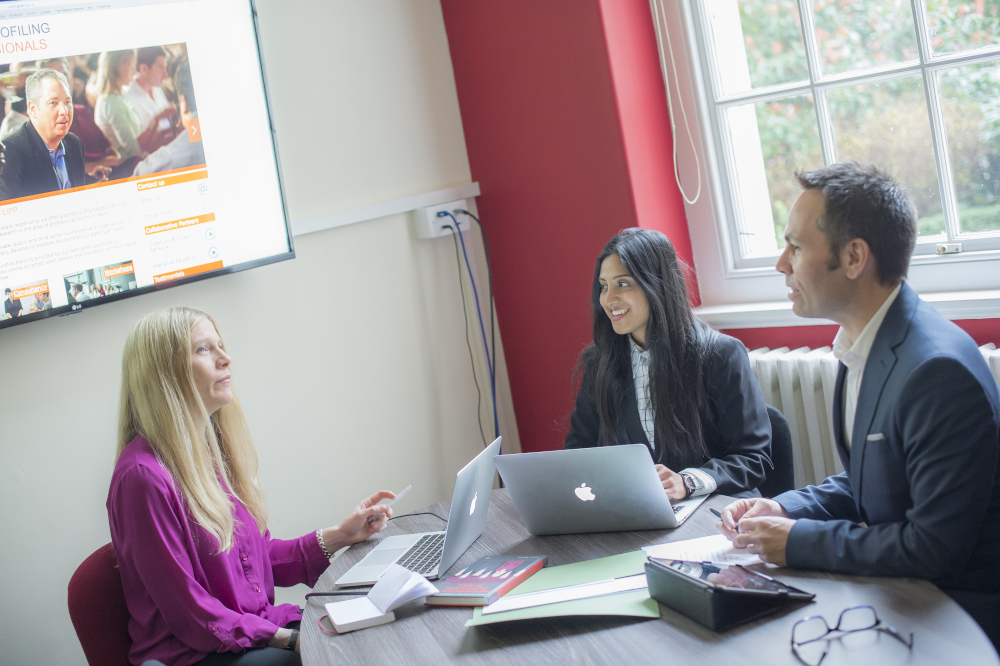 Three researchers sitting around a table in meeting with laptops and paperwork
