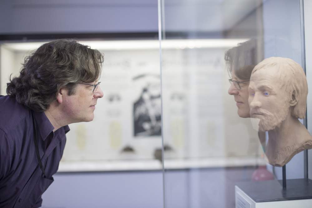 Researcher bending over and staring at head of statue in museum case