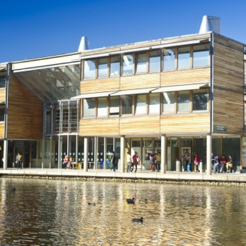 Wooden and glass buildings on Jubilee Campus set behind the lake with blue skies above