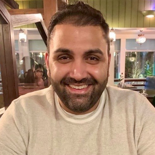 Sunny Sahdev with black short hair and beard and smiling wearing a cream jumper