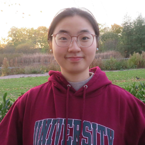 Xiaojie Cheng in a dark red hoodie, smiling wearing glasses and tied back black hair