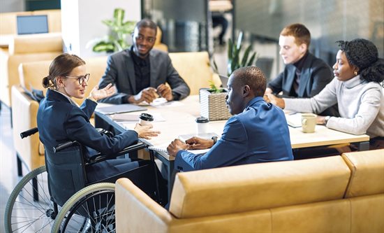 Group of professional people sat around a table having a discussion. One person is in a wheelchair.