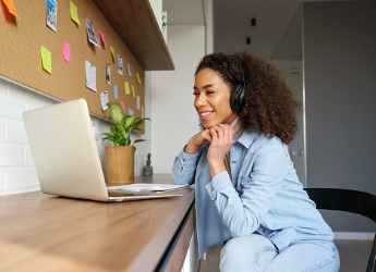 A smiling woman wearing headphones on laptop