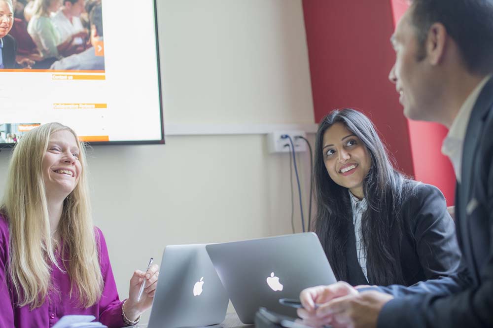 Three people sat in a meeting with laptops