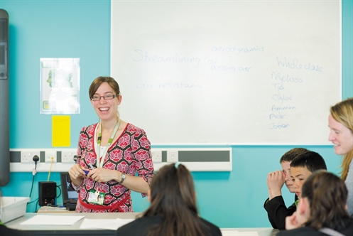 A teacher teaching a lesson to primary school students in a turquoise classroom.