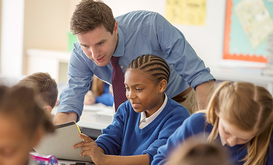 Male teacher helping a male pupil in a primary school classroom