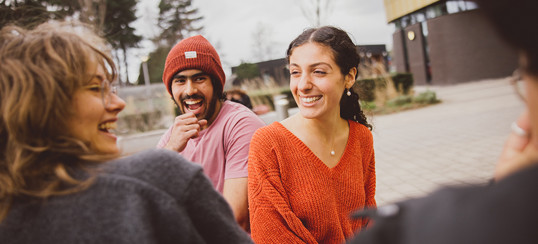A group of students outdoors on campus, laughing and chatting with each other