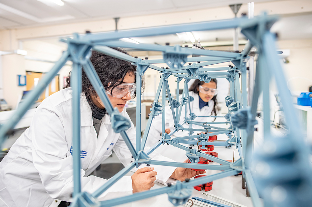Undergraduate students adding weights to a Pasco bridge loading demo