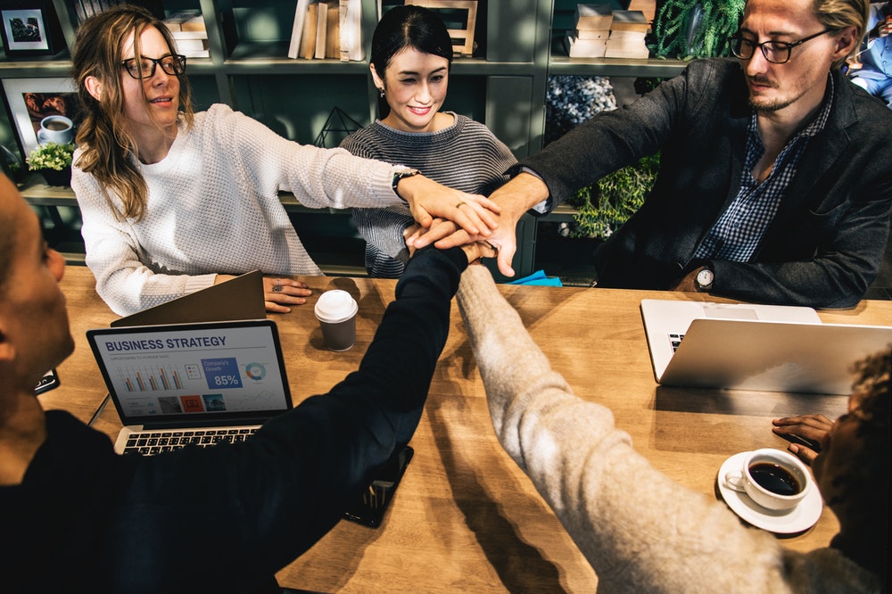 Group of people around a table holding hands forming teamwork