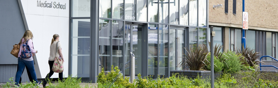 Two students walking in front of the entrance to the Medical School (Queen's Medical Centre)