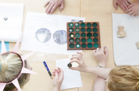 Overhead shot of a group of people looking at ancient coins, one person is wearing a paper hat