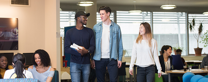 A diverse group of students laughing and chatting, carrying books