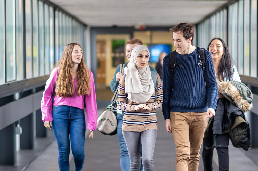 Students smile and chat as they walk across the bridge away from the Medical School