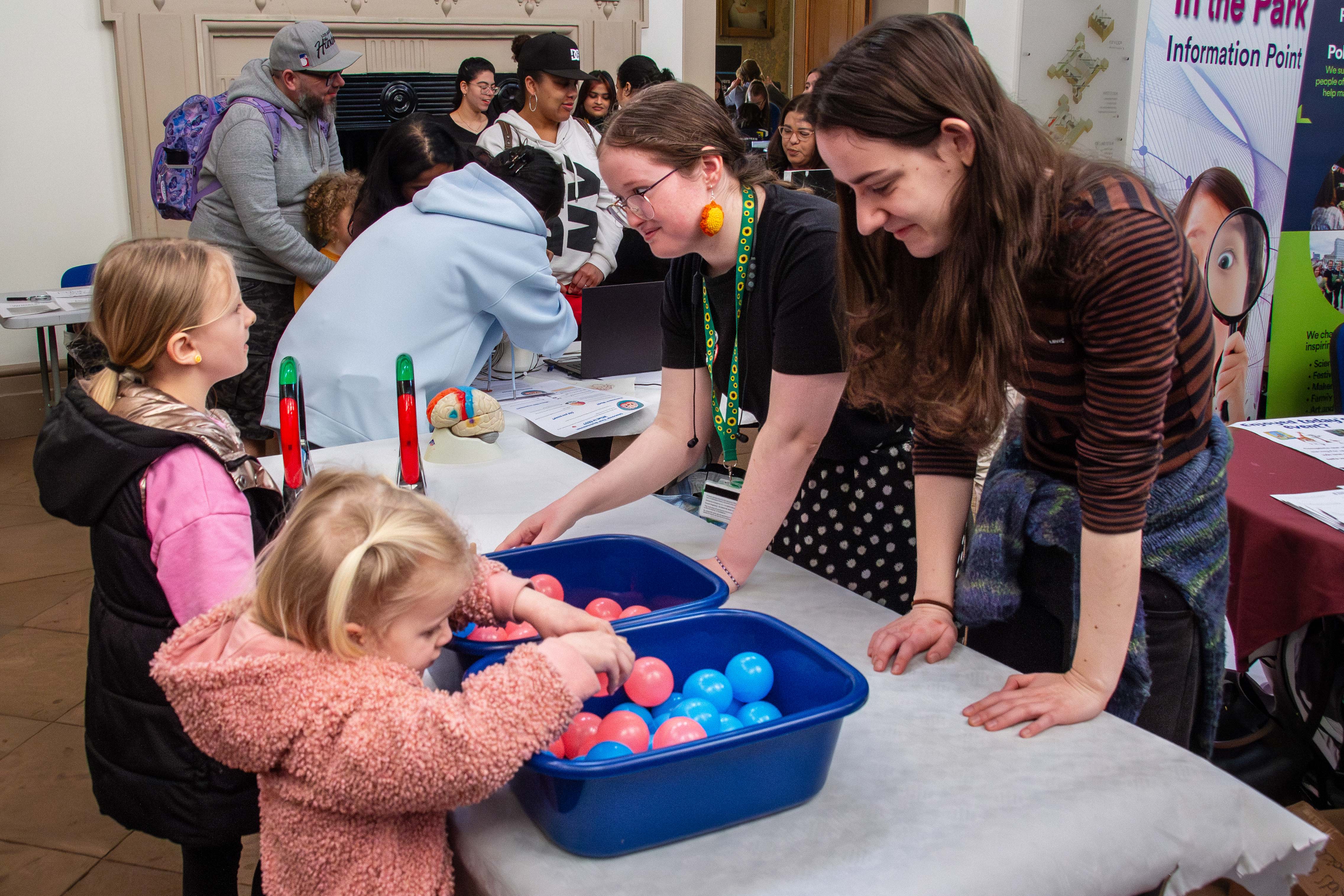 Two adult women showing two young girls how to play with plastic balls at Science in the Park 2025