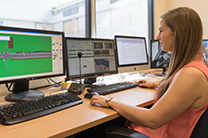 Female student sits at a desk working on a computer with three screens