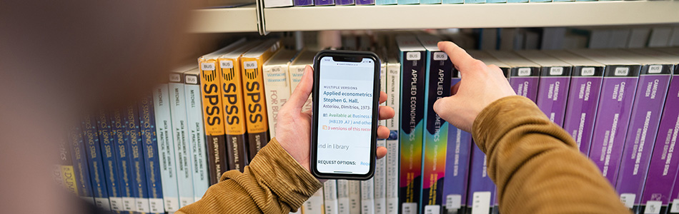 Student using a phone to find books on the library shelves