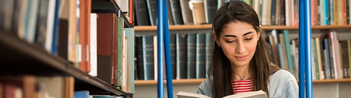 A student reading a book in front of book shelves in a library